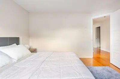 a white bedroom with a large white bed with a blue rug at Voltaire 2 Appartement 4,5 , 2ch Laval, Canada meublé in Laval