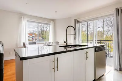 a kitchen with white cabinets and a large window at Voltaire 2 Appartement 4,5 , 2ch Laval, Canada meublé in Laval