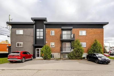 a brick building with two cars parked in a parking lot at Voltaire 2 Appartement 4,5 , 2ch Laval, Canada meublé in Laval