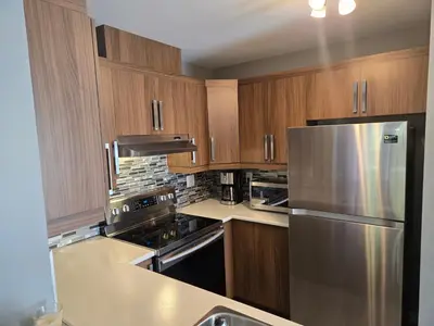 a kitchen with wooden cabinets and a stainless steel refrigerator at Cozy Digital Nomad Apartment in Montreal Riv-Sud in Brossard
