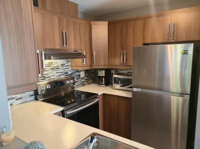 a kitchen with wooden cabinets and a stainless steel refrigerator at Cozy Digital Nomad Apartment in Montreal Riv-Sud in Brossard