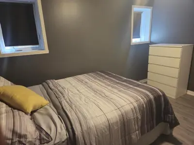 a bedroom with a bed with a yellow pillow and two windows at Cozy Digital Nomad Apartment in Montreal Riv-Sud in Brossard