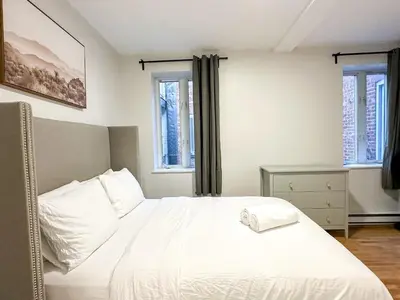 a bedroom with a white bed and two windows at Chic & Fully Furnished 2-Bedroom Apartment in Prestigious Westmount in Montréal