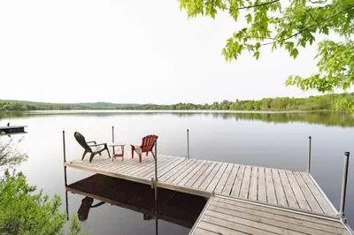 two chairs and a table on a dock on a lake at Mirror Lakefront and SPA - A Fleur D'eau in Dudswell