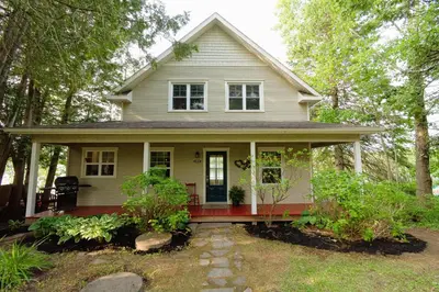 a white house with a red porch and trees at Mirror Lakefront and SPA - A Fleur D'eau in Dudswell