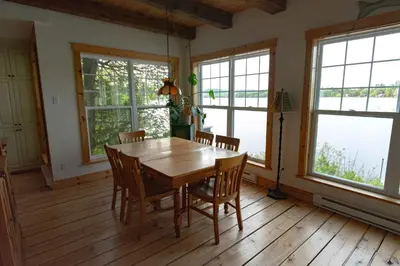 a dining room with a table and chairs and windows at Mirror Lakefront and SPA - A Fleur D'eau in Dudswell