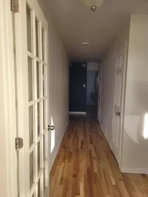 an empty hallway with an open door and wooden floors at Spacious and comfortable accommodation in Longueuil