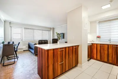 a kitchen with wooden cabinets and a living room at Downtown Montreal 2-Bedroom Gem near Bell Centre in Montréal