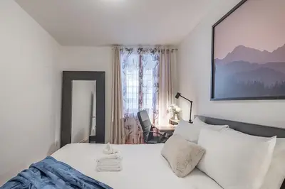 a white bedroom with a bed and a chair at Spacious 2BR Downtown - Vintage Charm Sleeps 10 in Montréal
