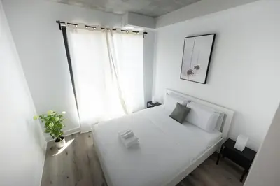 a white bedroom with a white bed and a window at Charming 1BR Old Port - Sofa Bed - Balcony with City View in Montréal