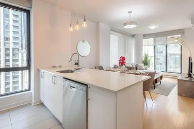 a white kitchen with a sink and a living room at Corner 2BR Old Port - Free Indoor Parking in Montréal