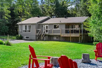 a house with a deck and red chairs in the yard at Lake - Spa - Pool Table - Chalet Ookpik in Potton