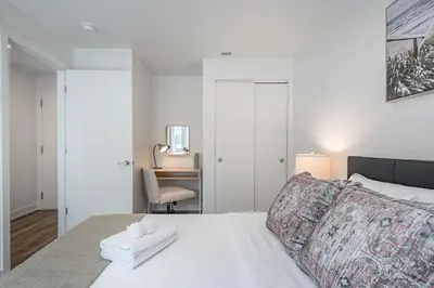 a bedroom with a white bed with a chair and a desk at Cozy Corner - Modern 1BR in MTL in Montréal