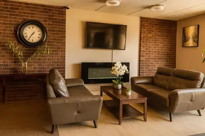 a living room with two chairs and a clock on a brick wall at Motel St-Eustache in Saint-Eustache