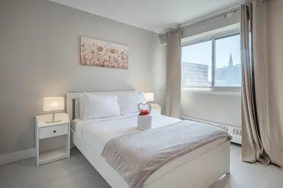 a white bedroom with a white bed and a window at Cozy 1BR - Heart of Montreal in Montréal
