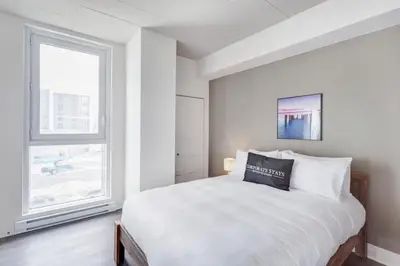 a white bedroom with a bed and a window at Corporate Stays Equinoxe 2 Bedroom in Laval