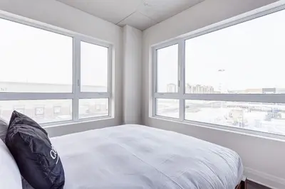 a bedroom with two large windows and a white bed at Corporate Stays Equinoxe 3 Bedrooms in Laval