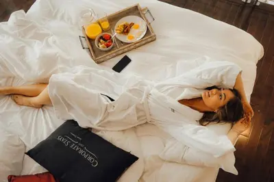 a woman laying on a bed with a tray of food at Corporate Stays Equinoxe 1 Bedroom in Laval
