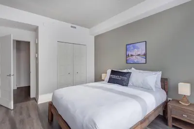a white bedroom with a large bed and a night stand at Corporate Stays Equinoxe 1 Bedroom in Laval