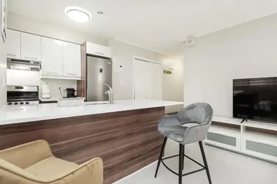 a kitchen with white cabinets and a chair and a tv at Séjour idéal au cœur de Montréal in Montréal
