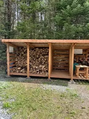 a wooden structure with a pile of fire wood at Chalet Le Mona in Notre-Dame-Des-Bois
