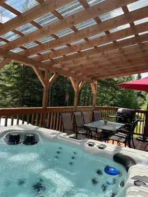 a hot tub under a wooden deck with a table at Chalet Le Mona in Notre-Dame-Des-Bois