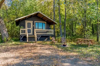 a cabin in the woods with a picnic table and a bench at chalet 5 Domaine de l'Archipel in Sorel