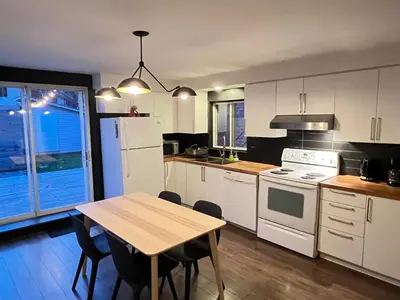 a kitchen with white cabinets and a table with chairs at Appartement Mid Century 2 Chambres avec Jardin in Montréal