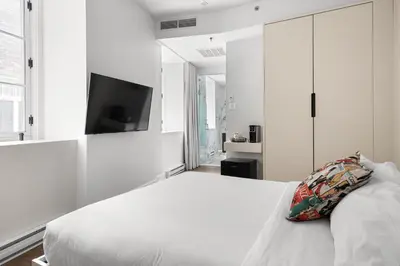a white bedroom with a bed and a tv on the wall at Nomade Saint Paul in Montréal