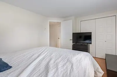 a white bedroom with a bed and a flat screen tv at Voltaire 1 Apartement 4,5 2ch Laval, Canada in Laval