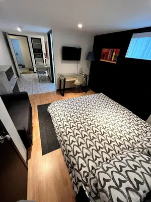 a bedroom with a bed and a room with a television at Charmant petit studio à 15 minutes de Montréal in Longueuil