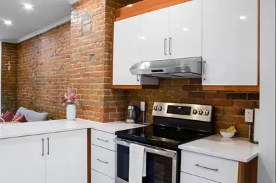a kitchen with white cabinets and a brick wall at Upscale 2BR Retreat - Parking - 2 Queen Suites in Montréal