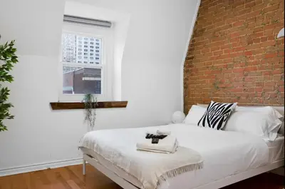a white bed in a room with a brick wall at Modern 2BR Haven - Prime Location in Montréal