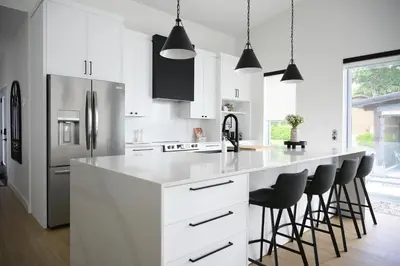 a kitchen with white cabinets and a large island with bar stools at Spa & Comfort - Chalet KG Petit lac Lambton in Lambton