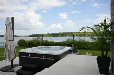 a hot tub sitting on a patio with a view of the water at Spa & Comfort - Chalet KG Petit lac Lambton in Lambton