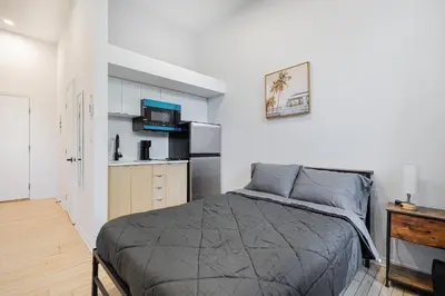 a bedroom with a bed and a kitchen with a refrigerator at Studio pour deux-location hebdomadaire avec parking gratuit in Montréal