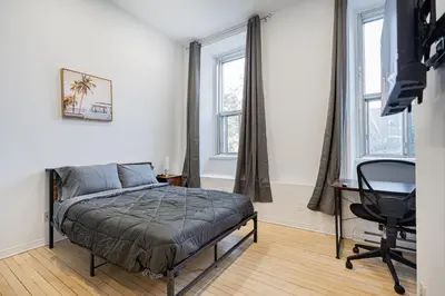 a bedroom with a bed and a desk and two windows at Studio pour deux-location hebdomadaire avec parking gratuit in Montréal