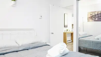 a white bedroom with a bed and a mirror at Appartement charmant proche des attractions in Montréal