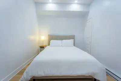 a white bedroom with a large bed and a lamp at Ambiance Urbaine À Montréal in Montréal