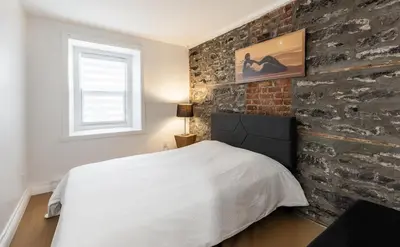 a bedroom with a white bed and a brick wall at Au coeur du plateau in Montréal