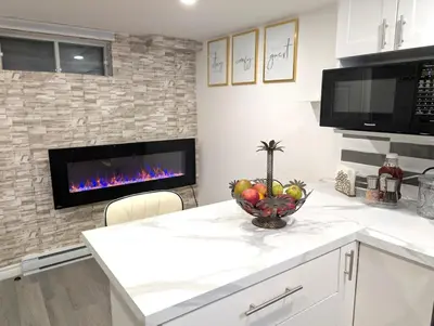 a kitchen with a fireplace and a bowl of fruit on a counter at Stylish & Modern Condo - FREE Parking & EV Chargers in Laval