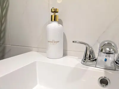 a white bottle of soap sitting on a bathroom sink at Stylish & Modern Condo - FREE Parking & EV Chargers in Laval
