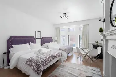 a white bedroom with two beds and a fireplace at Kozy Stays Drummond Modern apartments in Montréal