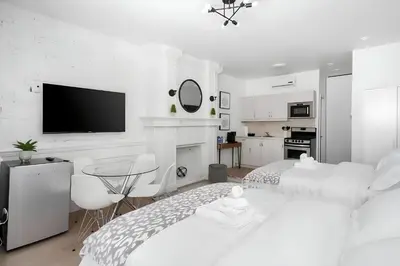 a white bedroom with a bed and a tv at Kozy Stays Drummond Modern apartments in Montréal