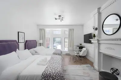 a white bedroom with a large bed and a fireplace at Kozy Stays Drummond Modern apartments in Montréal