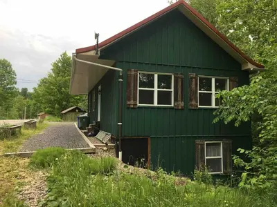 a green house with a road in front of it at Charming chalet for rent next to Owl Head SKI in Potton
