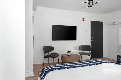 a bedroom with a bed and two chairs and a flat screen tv at Kozy Stays Penfield - Modern Rooms Heart of downtown in Montréal