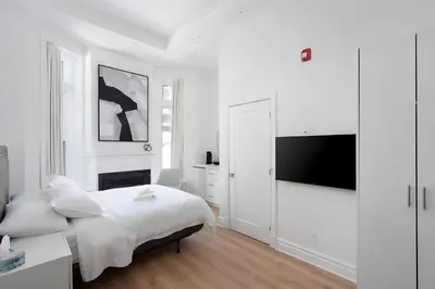a white bedroom with a bed and a flat screen tv at Kozy Stays Penfield - Modern Rooms Heart of downtown in Montréal