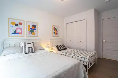 a white bedroom with two beds and paintings on the wall at 210 - Fantastic Neat 2BR with Parking, Gym, near DT&Airport in Montréal