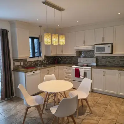 a kitchen with white cabinets and a table and chairs at Appartement cosy, comme à la maison in Montréal